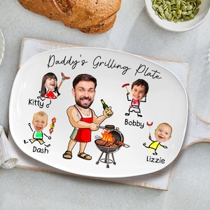 May include: White oval ceramic serving platter with a cartoon illustration of a family grilling. The text "Daddy's Grilling Plate" is written in black cursive. The illustration features a man with a red apron grilling, a woman holding a spatula, and three children.