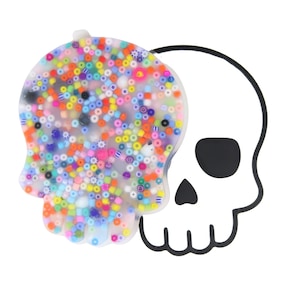 Può includere: Un vassoio in resina trasparente a forma di teschio riempito di perline colorate. Il vassoio è delimitato da un disegno di teschio nero.