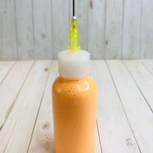 May include: A small bottle of orange paint with a white cap and a yellow needle applicator.
