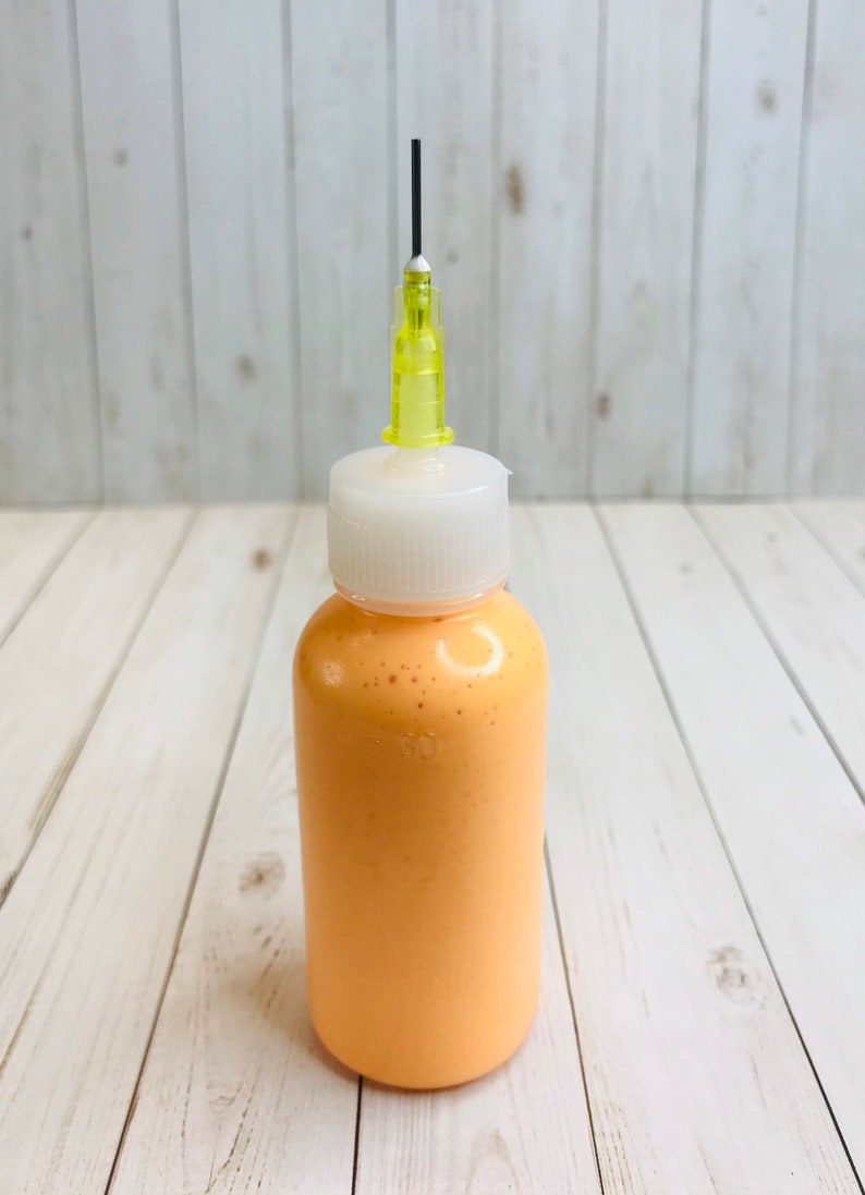 May include: A small bottle of orange paint with a white cap and a yellow needle applicator.