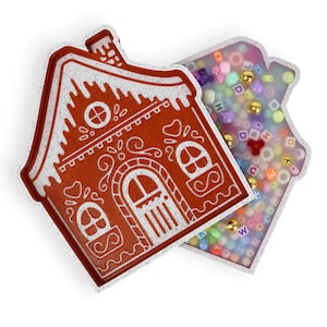 May include: A white and red gingerbread house shaped container with a clear lid filled with colorful alphabet beads.
