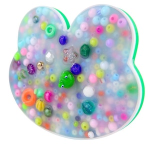 Pode incluir: Um ornamento em forma de coração de resina transparente cheio de contas coloridas, pequenos amuletos e uma figura de sapo verde.