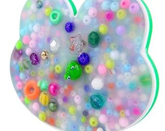 May include: A clear resin heart-shaped ornament filled with colourful beads, small charms, and a green frog figurine.