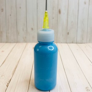Op de afbeelding: Een blauwe plastic fles met een witte dop en een gele naaldpunt. De fles is gemarkeerd met 30 ml, 15 ml en 10 ml.