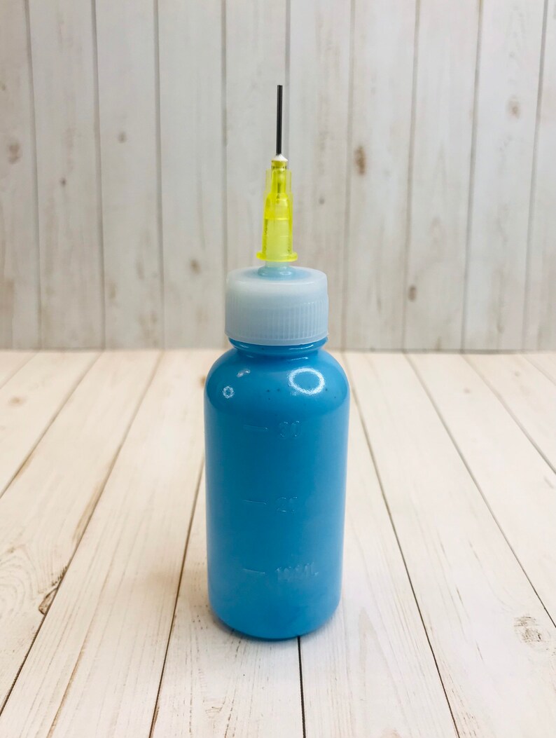 Op de afbeelding: Een blauwe plastic fles met een witte dop en een gele naaldpunt. De fles is gemarkeerd met 30 ml, 15 ml en 10 ml.