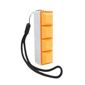 Puede incluir: Un pequeño juguete antiestrés naranja y blanco con una superficie texturizada y un cordón negro. El juguete tiene cuatro botones que se pueden presionar.