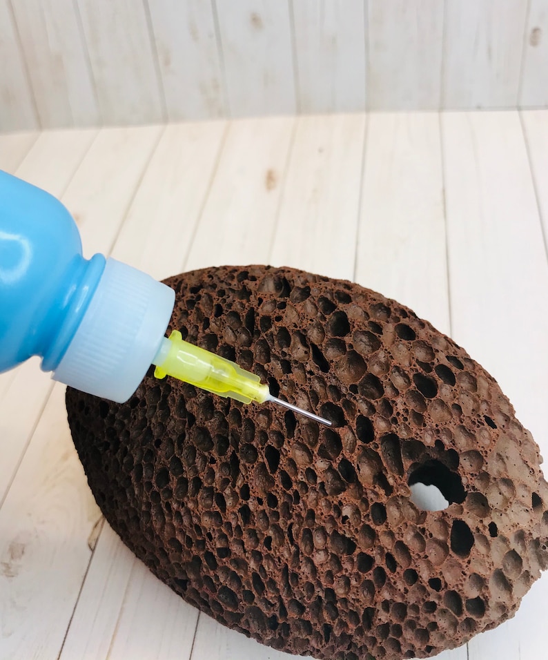 Op de afbeelding: Een blauwe plastic fles met een gele naald die in een bruine poreuze steen is gestoken.