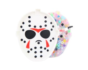 May include: A white plastic container with a black and white hockey mask design on the front. The container is open to reveal a clear plastic container filled with colorful beads.