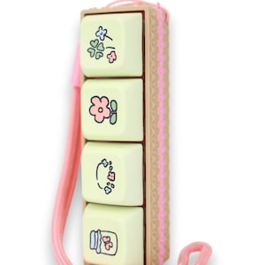 May include: A light green and pink key chain with four keycaps featuring floral and butterfly designs. The keycaps are attached to a brown and pink plastic frame. The key chain has a pink lanyard.