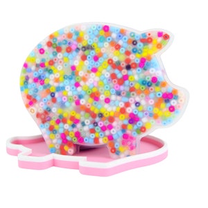 Può includere: Un salvadanaio a forma di maiale, riempito di perline colorate. La banca è realizzata in plastica trasparente e poggia su una base rosa con un bordo bianco. Le perline sono di vari colori, tra cui blu, giallo, rosso e verde.