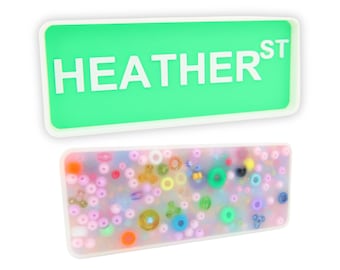 May include: A green rectangular tray with white lettering that reads "HEATHER ST". A second tray is filled with colourful beads and circles.