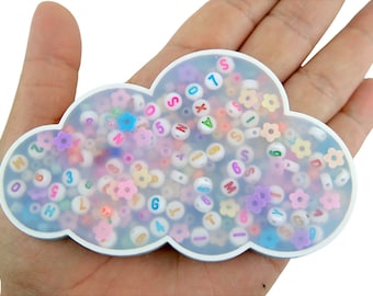 May include: A white cloud-shaped container filled with colourful alphabet and number beads. The beads are in various colours, including pink, blue, yellow, and purple.