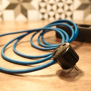 May include: A close-up of a blue electrical cord with a black plug. The cord is coiled and the plug is in focus.