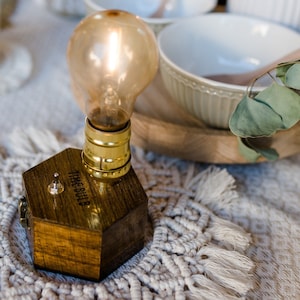 Könnte beinhalten: Ein Holz-Lampenhalter mit einer goldenen Glühbirne und einem Schalter mit der Aufschrift "The Bulb". Der Halter steht auf einem weißen gehäkelten Untersetzer.