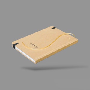 May include: A brown notebook with a black ribbon bookmark and a gold ribbon attached to the cover. The notebook has the text "TIMEBULB" printed on the front cover.