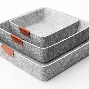 Puede incluir: Tres cestas de almacenamiento de fieltro gris con etiquetas de cuero marrón que dicen "Time Well Spent".