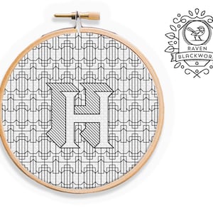 May include: Black and white embroidery hoop with a geometric pattern and the letter "H" in the center. The hoop is labeled "Raven Blackwork".