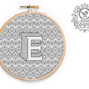 Könnte beinhalten: Ein Stickrahmen mit einem geometrischen Muster in Schwarzweiß, mit dem Buchstaben "E" in der Mitte. Der Rahmen ist aus Holz und hat eine Schraube aus Messing. Das Design stammt von Raven Blackwork.