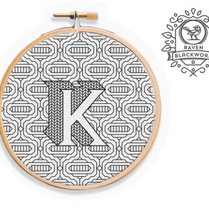 May include: Black and white embroidery hoop with a geometric pattern and the letter K in the center. The hoop is surrounded by a wooden frame. The text "Raven Blackwork" is visible in the upper right corner of the image.
