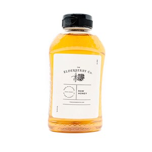 May include: A clear plastic bottle of raw honey from The Elderberry Co. The bottle has a black cap and a white label with text and a botanical illustration. The honey is a golden yellow color.