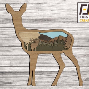 Könnte beinhalten: Ein hölzerner Ausschnitt eines Hirsches mit einer malerischen Berglandschaft im Inneren. Der Hirsch ist braun und die Landschaft ist eine Mischung aus Grün, Blau und Braun.