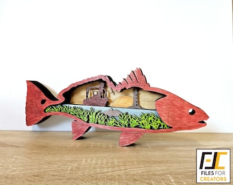 May include: A red fish cutout with a scene of a boat, a lighthouse, and a sunset inside. The fish is made of wood and has a detailed design.