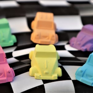May include: A set of six colorful toy cars, each painted in a different pastel color, including pink, blue, green, yellow, orange, and purple. The cars are arranged on a black and white checkered surface.