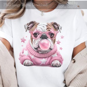 Könnte beinhalten: Ein weißes T-Shirt mit einer rosa und weißen Illustration eines Bulldogs, der eine rosa, sternförmige Sonnenbrille trägt und eine rosa Blase bläst. Der Bulldog trägt einen rosa Pullover mit weißen Sternen.