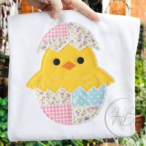 Puede incluir: Camiseta blanca con un diseño de aplique de un pollito amarillo saliendo de un huevo de retazos. La cáscara del huevo está decorada con telas de cuadros rosas, florales y lunares azules. El pollito tiene ojos negros y un pico naranja.