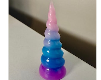 Peut inclure: Une sculpture de corne de licorne multicolore. La corne présente un dégradé de rose, de bleu et de violet. La base est violet foncé, passant au bleu, puis au rose à l'extrémité. La corne a un design en spirale.