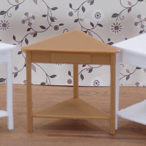 May include: Three miniature triangular tables. Two are white, and one is tan. Each table has a triangular shelf and three legs. The tables are arranged on a wooden surface in front of a floral patterned wallpaper.