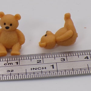 Puede incluir: Dos pequeños osos de peluche marrones, uno sentado derecho y el otro acostado de espaldas, se muestran junto a una regla que mide 5 centímetros.