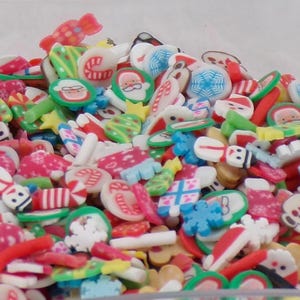 Puede incluir: Un gran surtido de abalorios de arcilla polimérica de temática navideña de colores. Los abalorios presentan varios diseños navideños, incluyendo bastones de caramelo, muñecos de nieve, Papá Noel y árboles de Navidad.