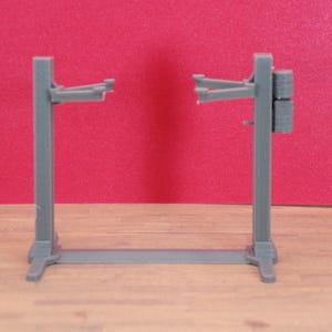 K&ouml;nnte beinhalten: Ein graues Modell einer Hebeb&uuml;hne f&uuml;r Autos, konzipiert zum Anheben von Fahrzeugen f&uuml;r Reparatur oder Wartung. Die Hebeb&uuml;hne hat zwei vertikale St&uuml;tzen, die durch eine horizontale Basis verbunden sind, mit verstellbaren Armen zum Anheben. Der Hintergrund ist einfarbig rot.