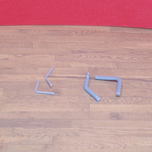 May include: Four light blue metal hooks are arranged on a wooden surface. Two hooks are L-shaped, and two are bent at an angle. The background features a red surface.