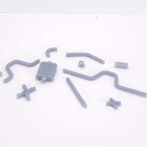 May include: A selection of grey car exhaust system parts, including pipes, a silencer, and connectors, arranged on a white surface. The components are made of a solid material and appear unused.