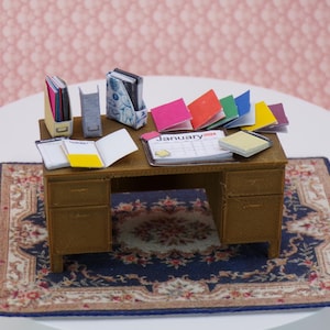 Puede incluir: Un escritorio de madera en miniatura con una alfombra de patrón azul y crema. El escritorio tiene un cajón a cada lado y está decorado con carpetas de papel de colores, cuadernos y un calendario que dice "Enero 2024".