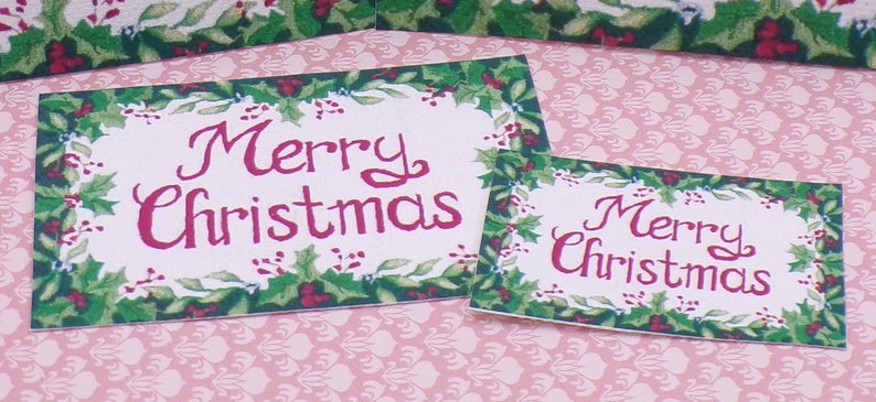 K&ouml;nnte beinhalten: Zwei rechteckige Weihnachts-Schilder mit gr&uuml;nem Stechpalmenrand und dem Text "Merry Christmas" in roten Buchstaben.