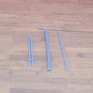 May include: Three light blue plastic pieces are arranged on a wooden surface. The pieces include a small, multi-pronged structure, a thick, rounded rod, and a thin, curved rod. The items appear to be components of a larger item.