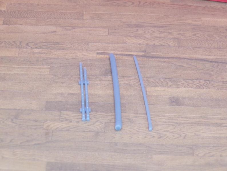 May include: Three light blue plastic pieces are arranged on a wooden surface. The pieces include a small, multi-pronged structure, a thick, rounded rod, and a thin, curved rod. The items appear to be components of a larger item.
