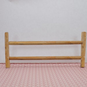 Puede incluir: Una valla de madera con dos rieles horizontales y postes verticales. La valla está hecha de madera natural y tiene un aspecto rústico.
