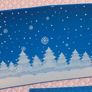 K&ouml;nnte beinhalten: Eine blaue Karte mit einer Winterszene aus wei&szlig;en B&auml;umen und Schneeflocken vor blauem Hintergrund.