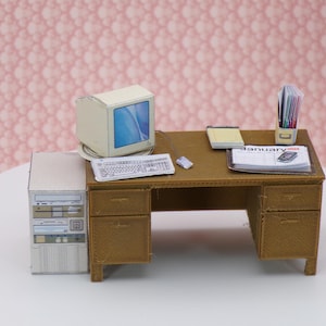 Puede incluir: Un escritorio en miniatura con una computadora beige, un teclado, un ratón y una pequeña carpeta de archivos etiquetada como "Enero". El escritorio tiene dos cajones y está hecho de madera marrón.