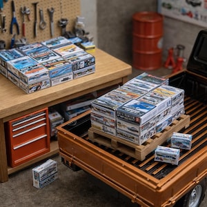May include: Miniature model car boxes stacked on a wooden table and in the bed of a brown pickup truck. The boxes are colorful with various car designs. A small orange toolbox is visible.