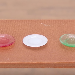 May include: Three small plates, one red, one white, and one green, are arranged in a row on a brown surface.
