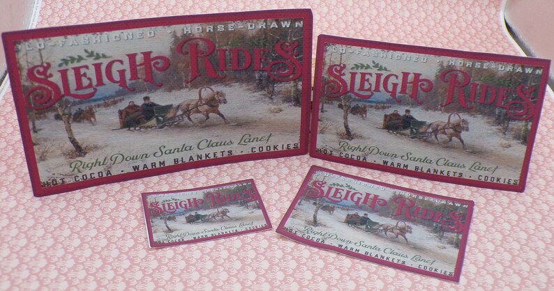 K&ouml;nnte beinhalten: Vier vintage rote und wei&szlig;e Schilder, die mit Pferden gezogene Schlittenfahrten bewerben. Die Schilder zeigen eine Winterszene mit einem von Pferden gezogenen Schlitten und dem Text "Old Fashioned Horse Drawn Sleigh Rides", "Right Down Santa Claus Lane! Hot Cocoa - Warm Blankets - Cookies".
