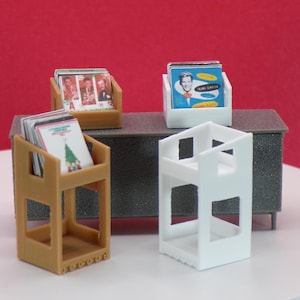 May include: Miniature display stands holding album covers. The stands are in various colors: tan, white, and brown. The album covers feature images of performers and holiday themes. The background is a solid red.