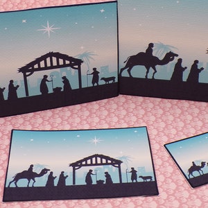 K&ouml;nnte beinhalten: Vier verschiedene Gr&ouml;&szlig;en von Weihnachtskarten mit einer Silhouette der Weihnachtsgeschichte mit einem Stern am Himmel. Die Karten sind auf blauem und wei&szlig;em Papier gedruckt.