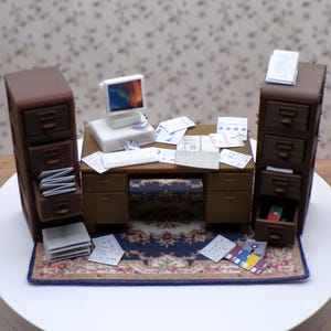 May include: A miniature office desk set featuring a computer, two filing cabinets, and a rug. The desk is brown with a wood grain finish. The filing cabinets are brown with drawers. The rug is patterned with a blue, white, and brown design. The computer is white with a black screen.