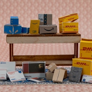 May include: A collection of miniature cardboard boxes, including DHL, UPS, and Priority Mail, arranged on a wooden shelf and a patterned rug. The boxes are various sizes and colours, with some stacked on top of each other.